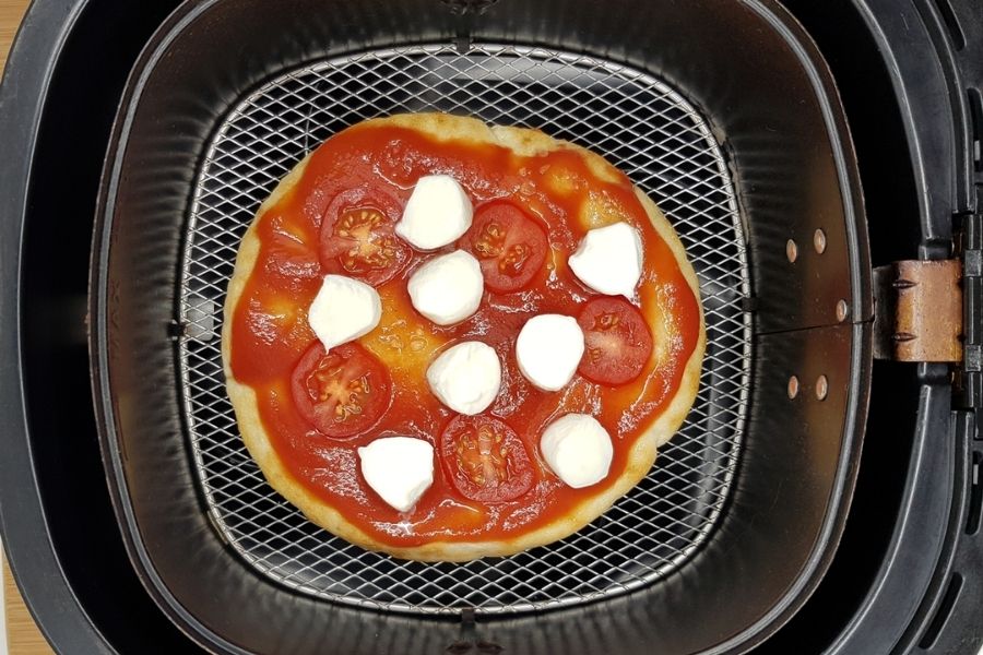Uncooked flatbread pizza in air fryer basket. 